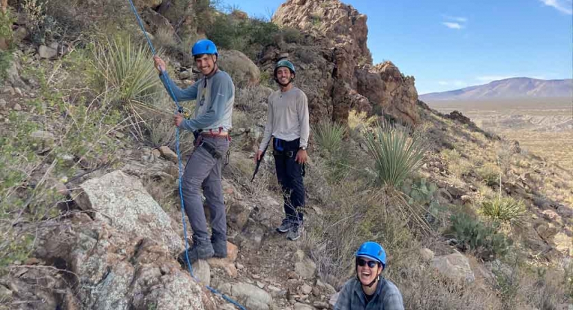 a group of students smile at the camera during a rock climbing portion of an outward bound trip
